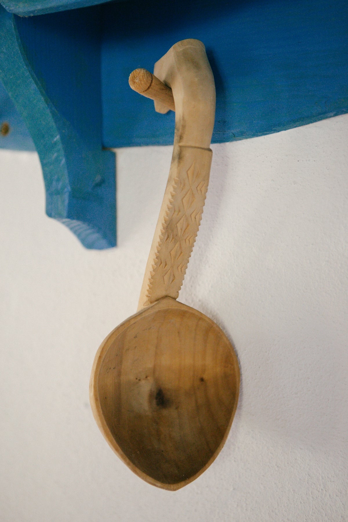 A wooden spoon hanging from a blue shelf