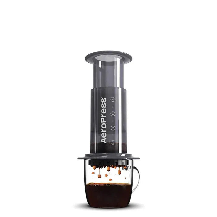 Aeropress coffee maker dispensing coffee into a glass mug on a white background