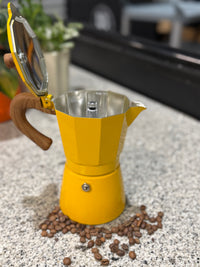 Thumbnail for Yellow espresso maker with wooden handle on a speckled countertop with coffee beans around it.