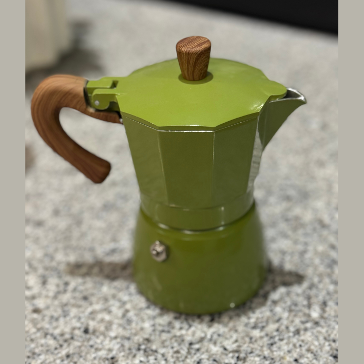 Green espresso maker with wooden handle and lid on a speckled countertop