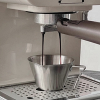 Thumbnail for A close-up of an espresso machine dispensing dark coffee into a stainless steel measuring cup on a drip tray.