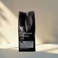 Thumbnail for Black coffee bag labeled 'Eighteen Grams' on a light background. Black Ebony coffee beans with a strong roasted profile, heavy body, very low acidity and intense cocoa nib, toasted coffee and bitter dark chocolate flavour.