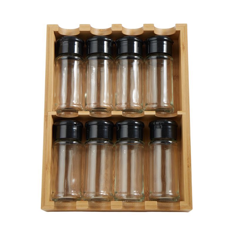 Set of glass spice jars with black lids in a wooden organizer on a white background