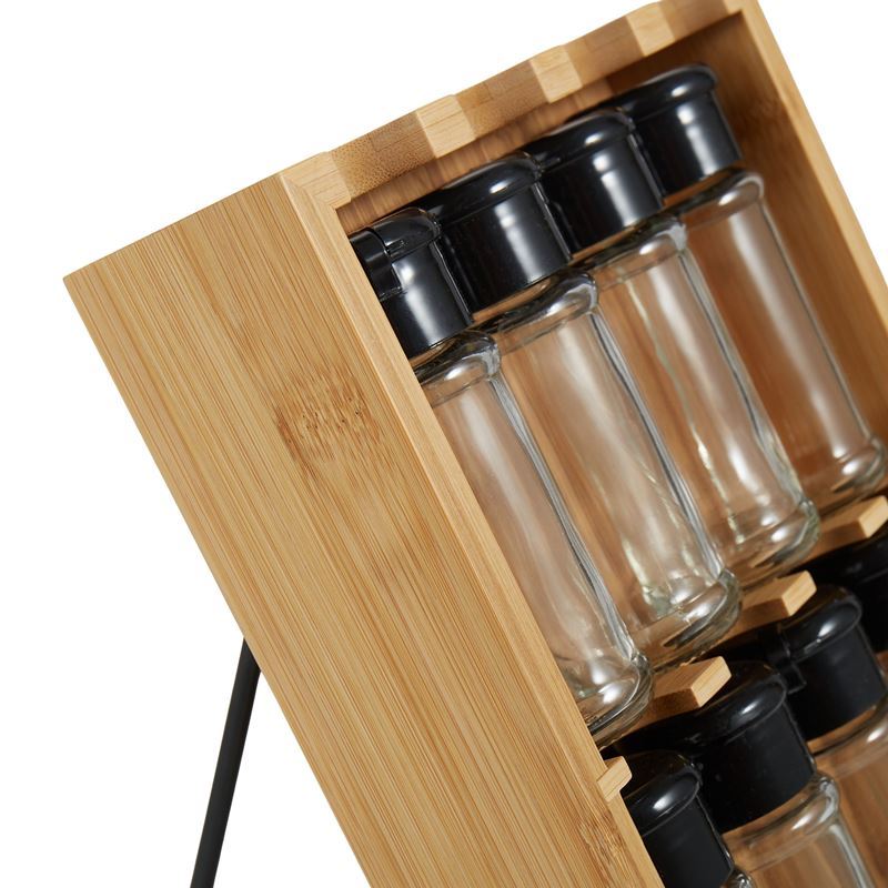 Set of glass spice bottles with black lids in a wooden holder on a white background