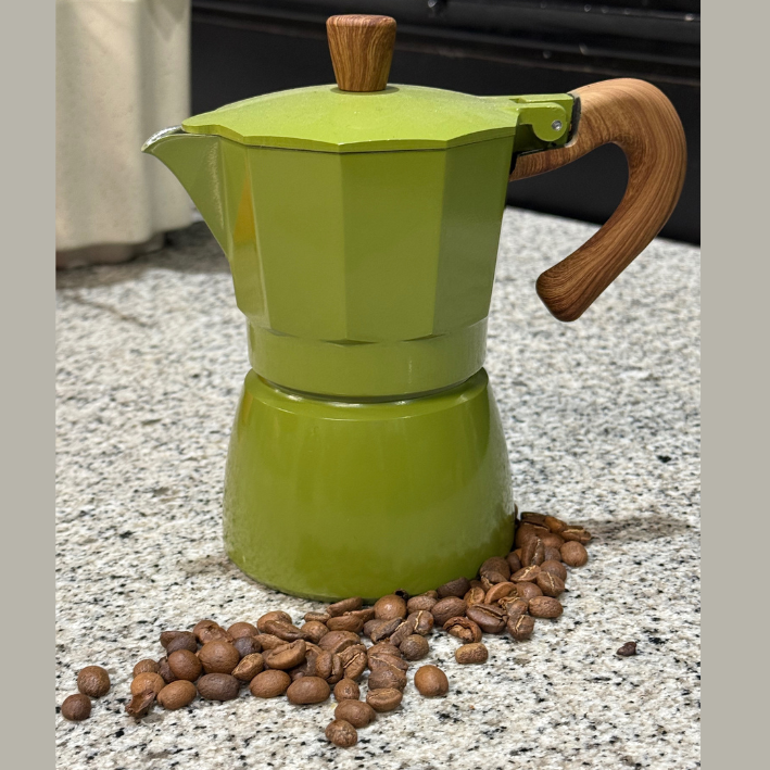 Green espresso maker with wooden handle and top on a surface with coffee beans around it.