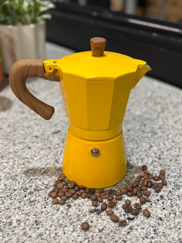 Yellow espresso maker with wooden handle on a surface with coffee beans